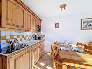 A kitchen with wooden cabinets, a tiled backsplash, a stove, and a dining table set for two. - Spacious Apartment with Balcony and Pool near Slopes (Les Menuires)