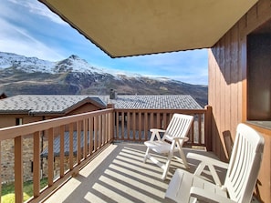 A balcony with wooden railings, two white plastic chairs, and a view of snow-capped mountains. - Spacious Apartment with Balcony and Pool near Slopes (Les Menuires)