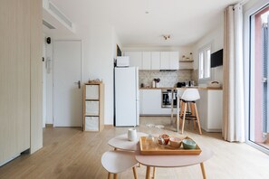 A modern kitchen with white cabinets, a built-in oven, and a dining area with a table and chairs. - Le Cocon Mouginois - calme sur la Côte d'Azur (Mougins)