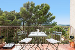 A balcony with a table and chairs, overlooking a forested area. - Le Cocon Mouginois - calme sur la Côte d'Azur (Mougins)