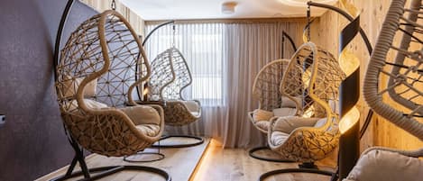 A room with hanging chairs, wooden flooring, and a large window with curtains.