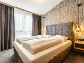 Quarto de hotel com uma cama grande, cortinas, cabeceira e iluminação fixada na parede.