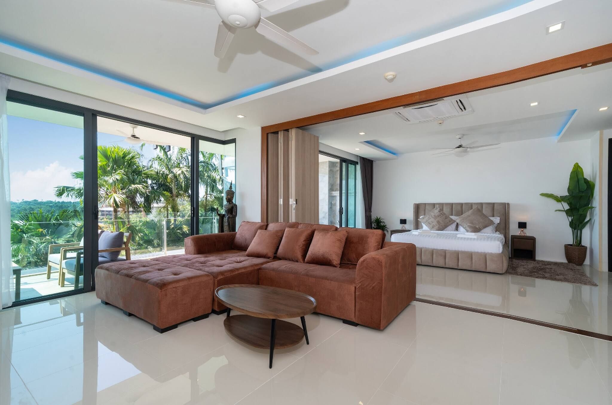 A modern living room with a sectional sofa, a coffee table, and a view of a bedroom with a bed and nightstands.