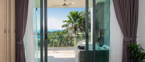Un dormitorio moderno con un puerta corrediza de vidrio que da a un balcón con vistas a palmeras y al océano.