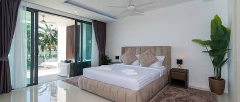 Une chambre à coucher moderne avec un grand lit, un ventilateur de plafond, une plante en pot et une vue sur l’extérieur.