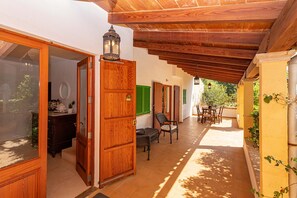 Uma área externa coberta com teto de madeira, mesa de jantar com cadeiras e vista para o verde.