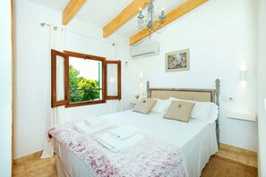 Un dormitori amb un llit, una finestra amb cortines, una làmpada de cristall i un quadre al mur.
