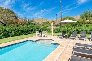 Ein Pool mit gewölbter Kante, umgeben von einer Terrasse mit Stühlen und Sonnenschirm.