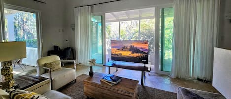 Una sala de estar con televisor, sofá, mesa de centro y vistas a un paisaje a través de las ventanas.