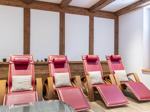 Eine Reihe von Loungestühlen mit Holzrahmen, roten Kissen und weißen Kopfkissen, angeordnet an einer Wand mit Holzbalken.
