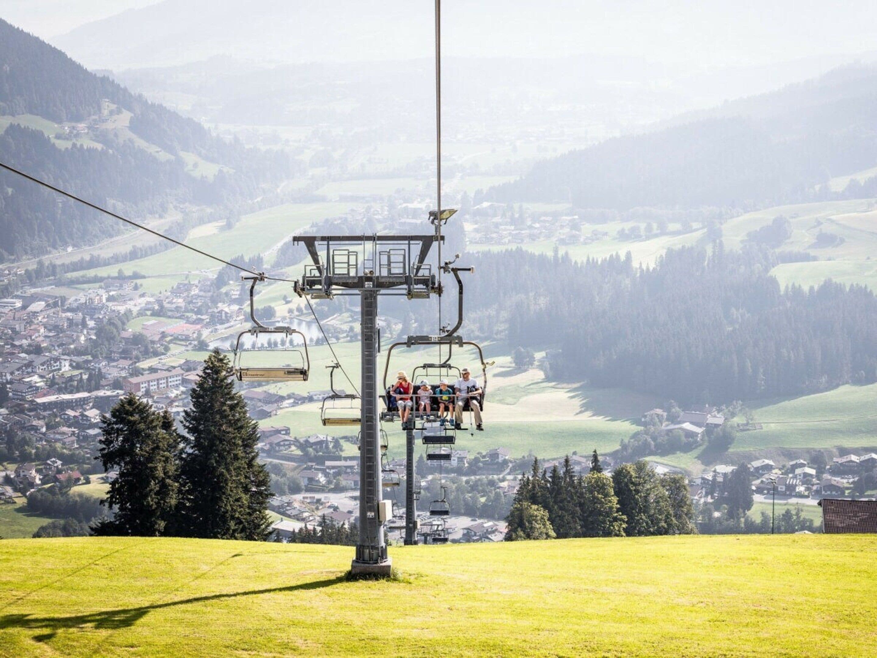 A ski lift with passengers, a town in the background, and a mountainous landscape.