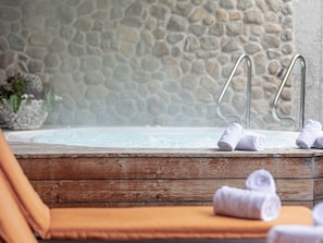 A stone wall, a hot tub with metal steps, and rolled towels on a wooden bench. - Penthouse With 2 Bedrooms (Reith bei Kitzbuehel)