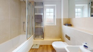 Badeværelse med glasvæg omkring bruseren, toilet, håndvask og håndklædestang.