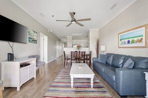 A modern living room with a flat-screen TV, a ceiling fan, a dining area with a table and chairs, and a gray sofa. - Marsh Views| Folly Beach| Sleeps 8 (Folly Beach)