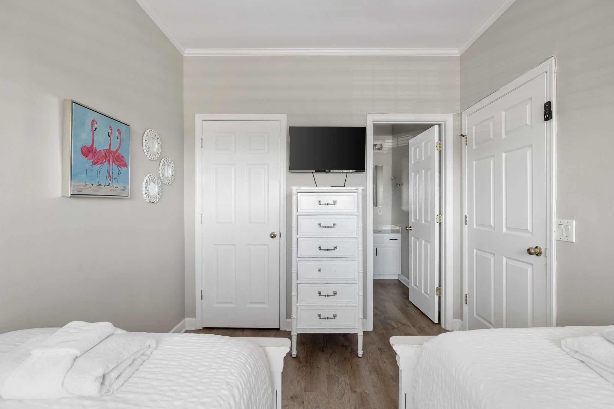 A bedroom with two beds, a dresser, a television, and a door leading to a bathroom.
