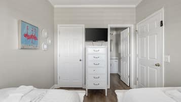 A bedroom with two beds, a dresser, a television, and a door leading to a bathroom.