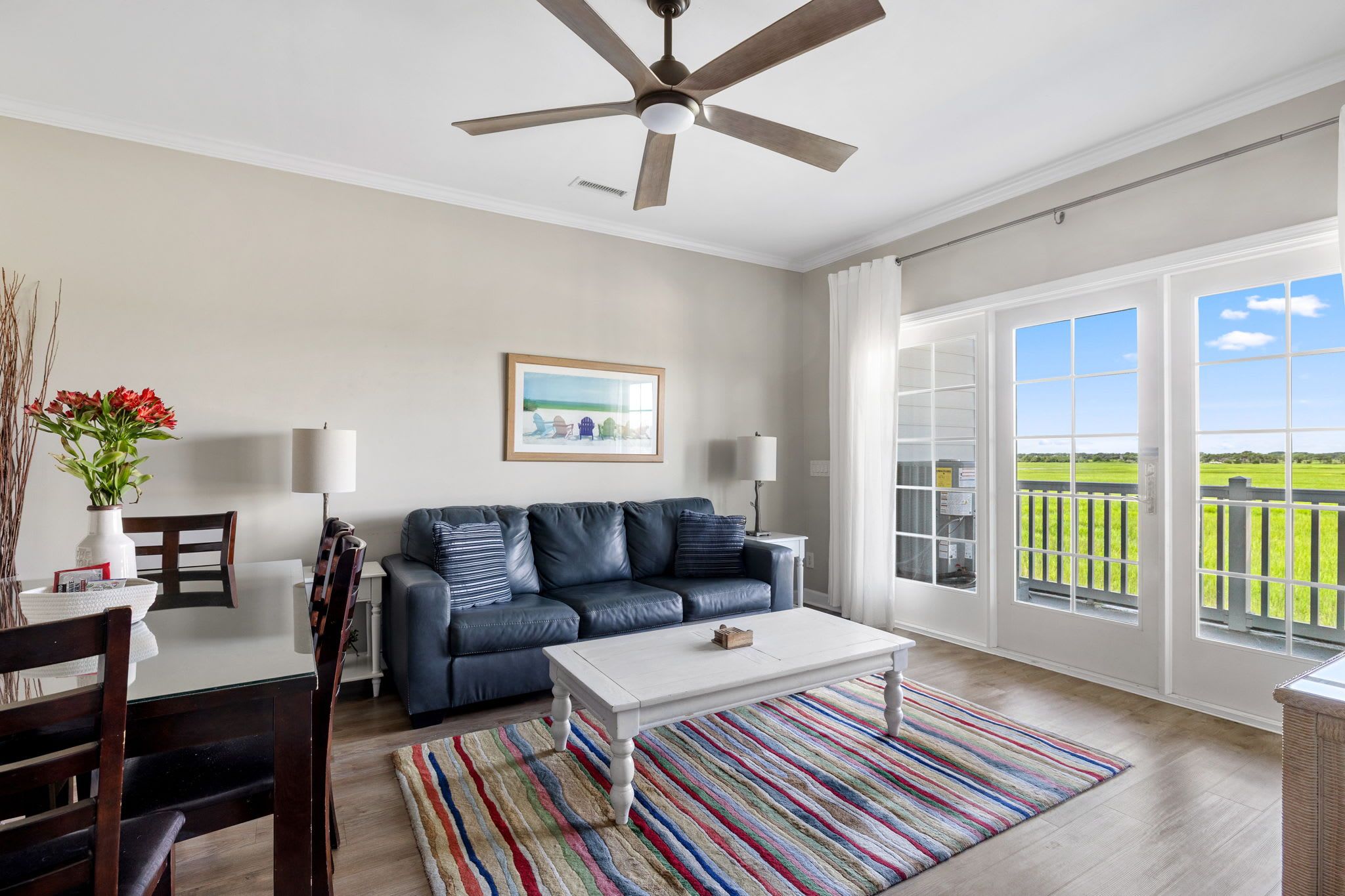 A spacious living room with a dark leather sofa, a white coffee table, and a colorful striped rug.