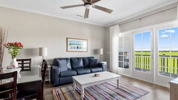 A spacious living room with a dark leather sofa, a white coffee table, and a colorful striped rug.