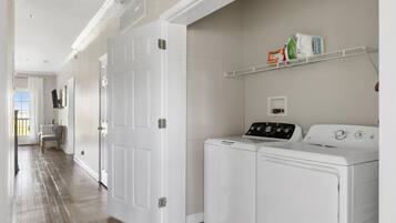 A laundry room with a washer and dryer, a shelf with laundry supplies, and a door leading to another room.