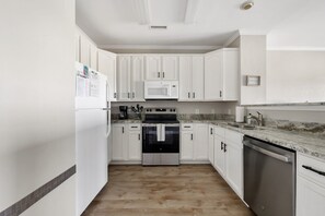A kitchen with white cabinets, a stainless steel dishwasher, a microwave, and an oven. - Marsh Views| Folly Beach| Sleeps 8 (Folly Beach)
