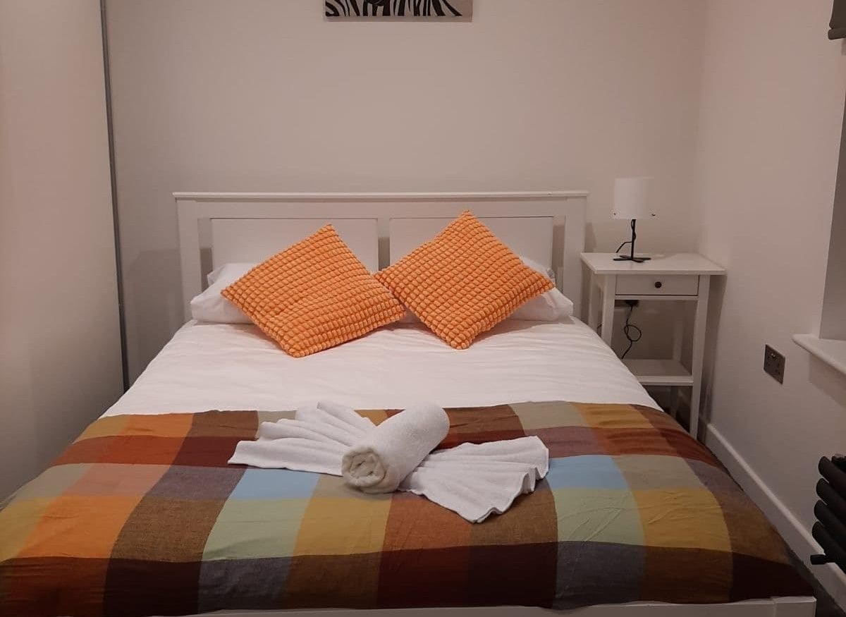 Un lit bien fait, recouvert d’une courtepointe aux couleurs vives, avec deux oreillers orange et une serviette blanche enroulée.