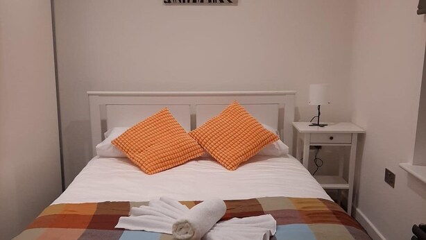 Een net opgemaakt bed met een kleurrijke quilt, twee oranje kussens en een opgerolde witte handdoek.