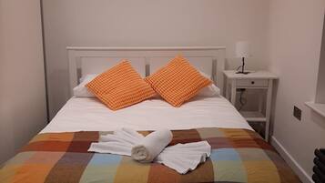 Un lit bien fait, recouvert d’une courtepointe aux couleurs vives, avec deux oreillers orange et une serviette blanche enroulée.