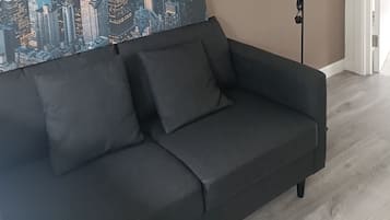 Un canapé de couleur sombre, agrémenté d’un coussin, placé contre un mur orné d’une fresque représentant un paysage urbain.