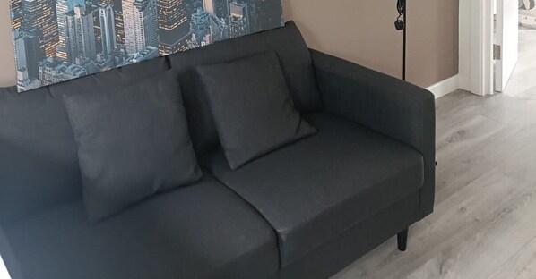 A dark-colored sofa with a cushion, positioned against a wall with a cityscape mural.