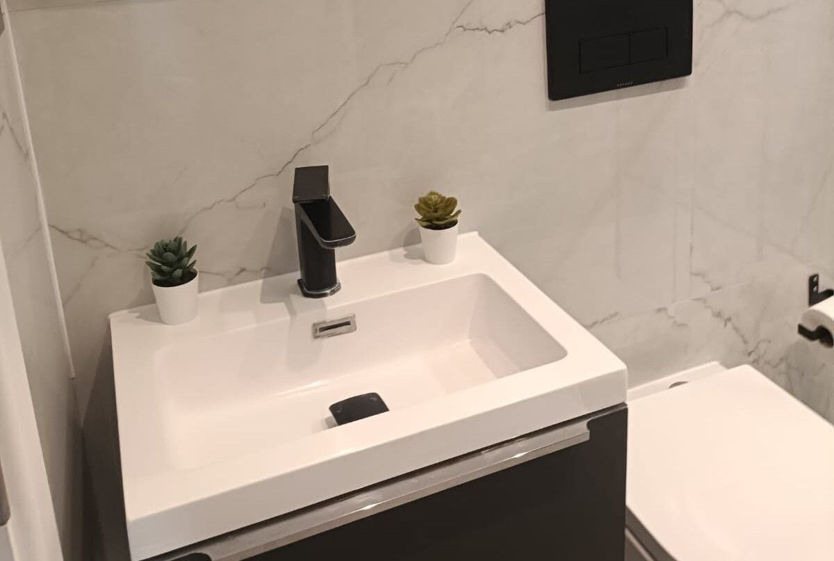 A modern bathroom with a white sink, a black faucet, and two small potted plants.