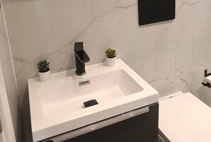 A modern bathroom with a white sink, a black faucet, and two small potted plants.