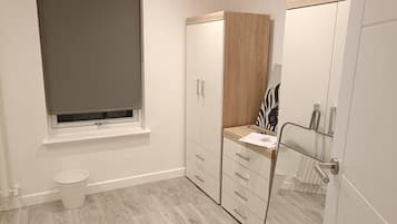 Une salle de bain comprenant des toilettes, une fenêtre avec un store, un meuble en bois avec des tiroirs et un miroir à motifs zébrés.