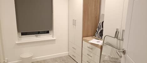 A bathroom with a toilet, a window with a blind, a wooden cabinet with drawers, and a mirror with a zebra print.