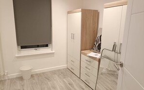 A bathroom with a toilet, a window with a blind, a wooden cabinet with drawers, and a mirror with a zebra print.