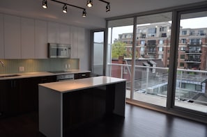 Een moderne keuken met een groot schiereiland, roestvrijstalen apparatuur en uitzicht op een woongebouw door grote ramen.