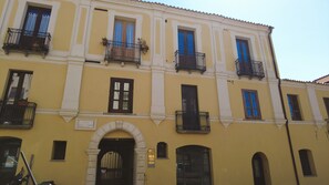 A yellow building with multiple balconies, a central archway, and a door with a number plaque.