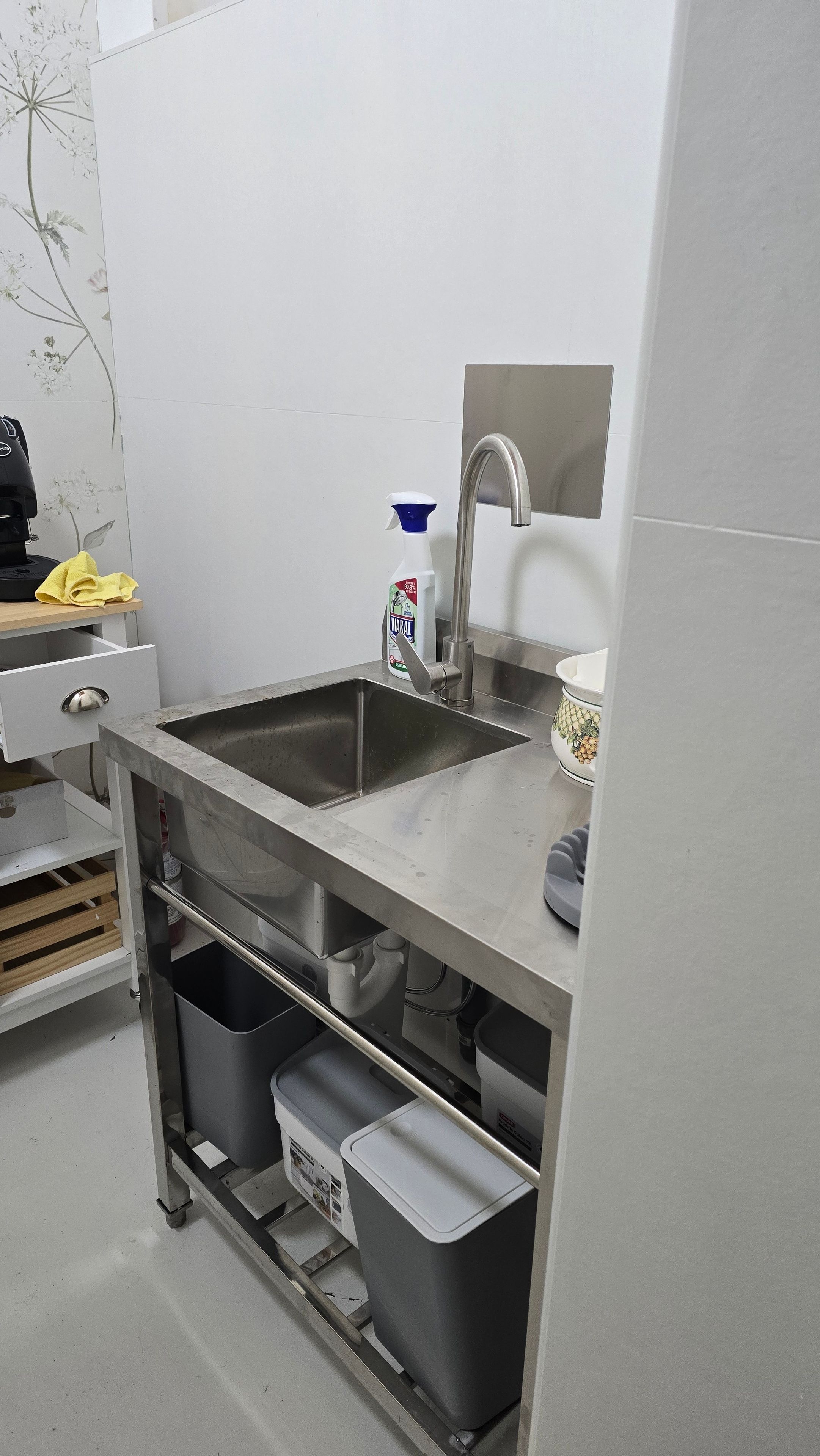 A kitchen with a stainless steel sink, a coffee machine, and a bottle of cleaning spray.