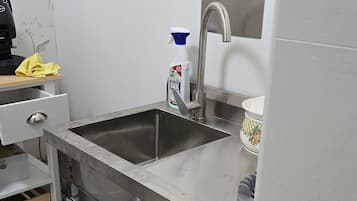 A kitchen with a stainless steel sink, a coffee machine, and a bottle of cleaning spray.