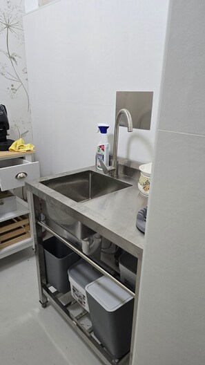 A kitchen with a stainless steel sink, a coffee machine, and a bottle of cleaning spray.
