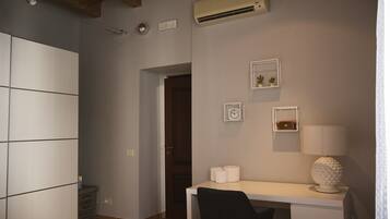 Un dormitorio con cama, escritorio, silla, aire acondicionado de pared y puerta que da a otra habitación.