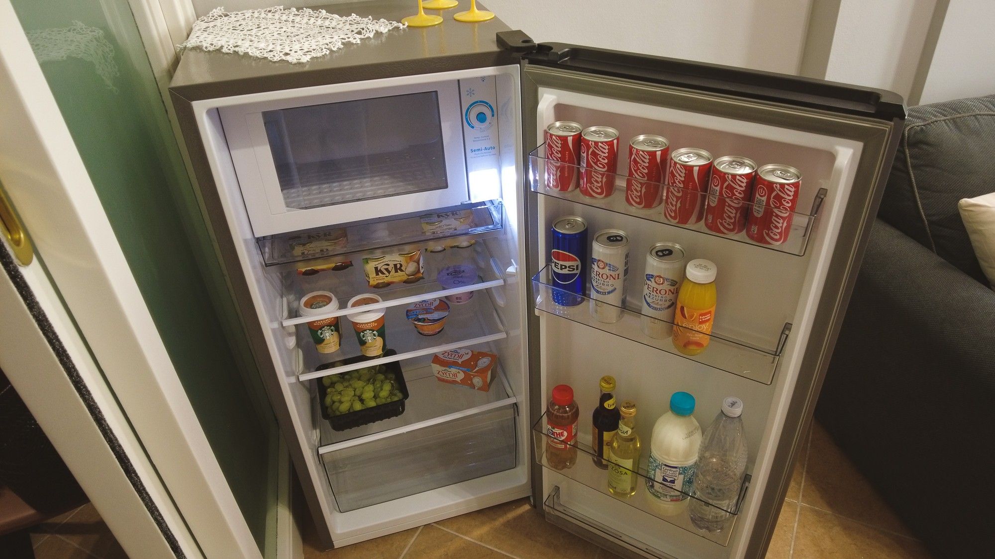 A refrigerator with a microwave on top, stocked with beverages, condiments, and food items.