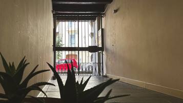 A corridor with a metal gate leading to an outdoor area with a red chair and a bicycle.