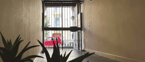 A corridor with a metal gate leading to an outdoor area with a red chair and a bicycle.