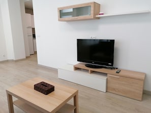 Ein modernes Wohnzimmer mit einem Flachbildfernseher, Holzmöbeln und einem kleinen Tisch mit einem Ziegelobjekt darauf.