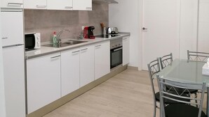 Una cuina moderna amb armaris blancs, forn integrat i zona de menjador amb taula de vidre i cadires metàl·liques.