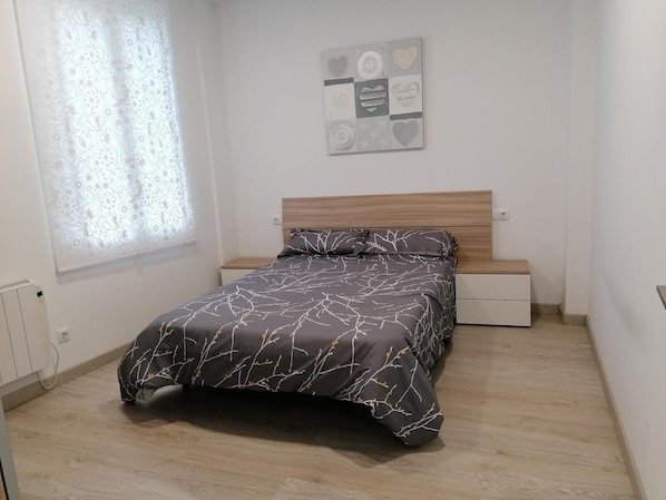 Ein Schlafzimmer mit einem Bett, einem Nachttisch, einer Kommode, einem Fenster mit Vorhängen und einer Wanddekoration.