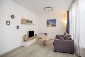 Un salon moderne avec un téléviseur à écran plat, un meuble en bois, un tableau représentant une scène de plage, un canapé et une lampe.