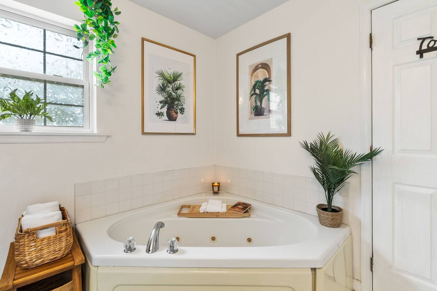 A bathroom with a freestanding bathtub, a window with a view, and two framed botanical prints on the wall.