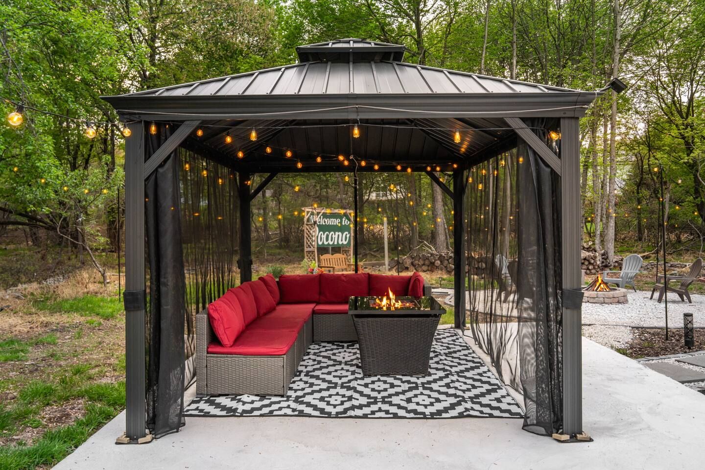 A covered outdoor seating area with a fire feature, surrounded by trees.