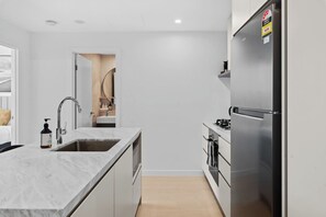 A modern kitchen with a marble countertop, stainless steel appliances, and a built-in oven. - Stylish 1BR in the Heart of Broadbeach (Broadbeach)